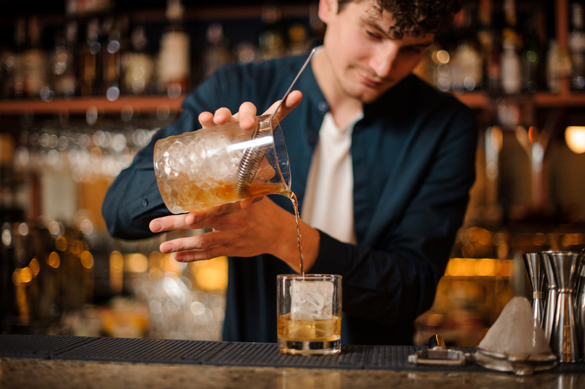 barman prepares an Old Fashioned alcoholic cocktail, adding whiskey to the ice